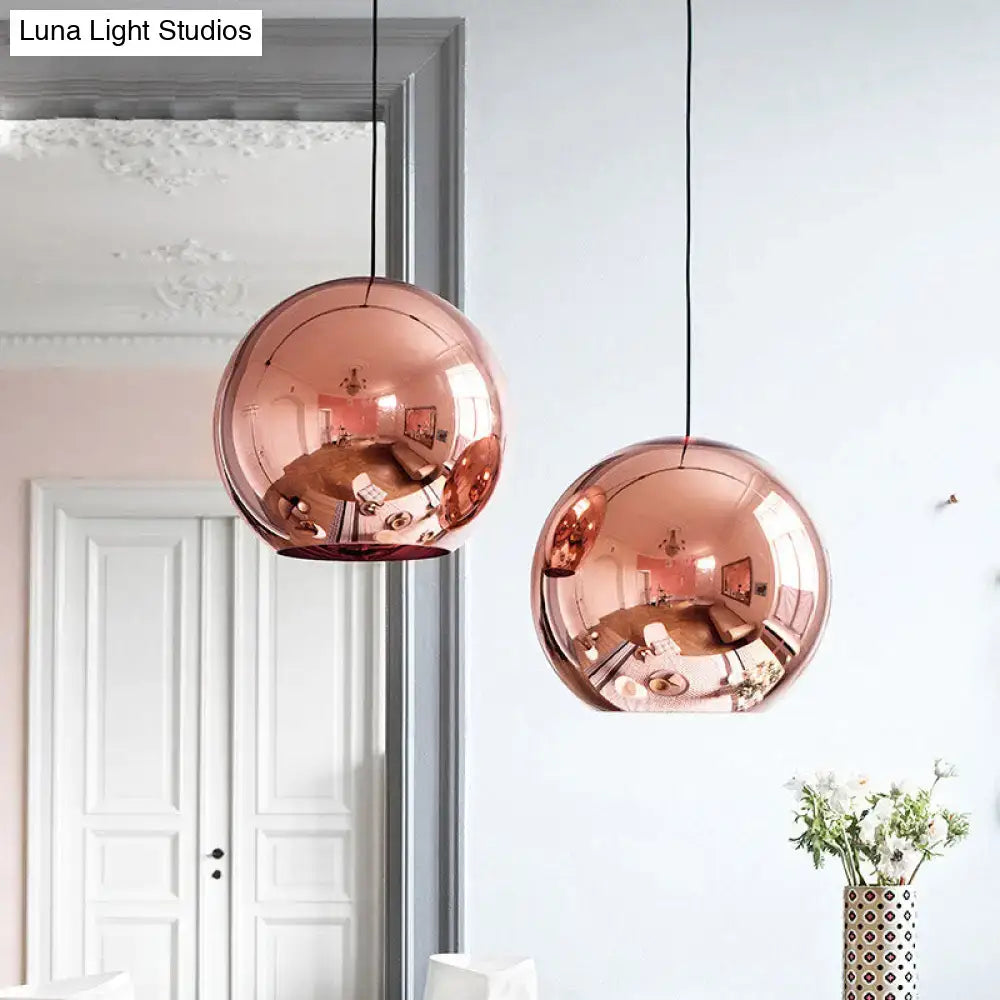Two rose gold copper sphere pendant lights with polished surfaces hang from black cords for kitchen bar use
