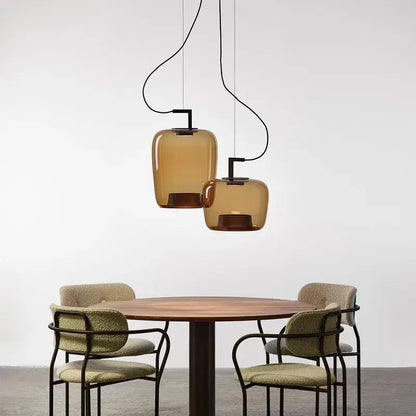 Two amber glass brokis glass pendant lamps with black metal fixtures hang above a wooden dining table decorbites brokis glass