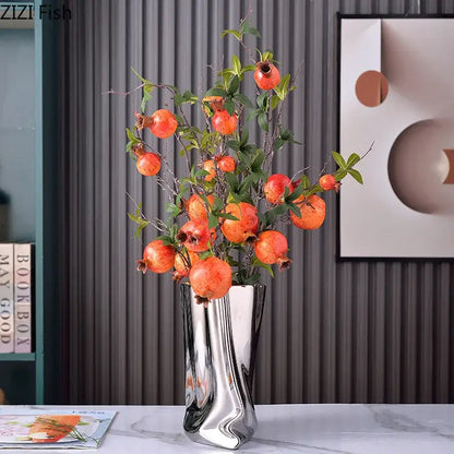 A sleek silver ceramic vase with pleated texture holds artificial pomegranates and green leaves for living room decor
