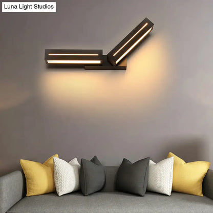 Modern black wall mounted light with two angled illuminated rectangular panels casting a warm glow for bedroom use