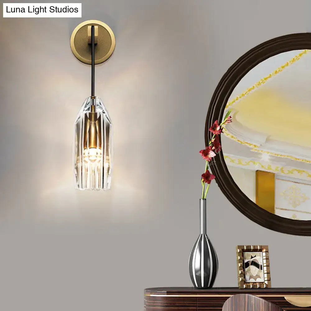 Modern single light brass wall sconce with a gold base black stem and clear crystal faceted glass shade for bedroom use