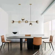 Modern smoke gray and gold linear design pendant light with brass and glass spherical bulbs above dining table
