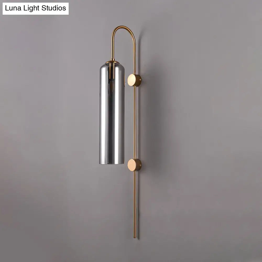 Modern smoke gray glass wall light with sleek cylindrical chrome shade and slender brass arms for living room use