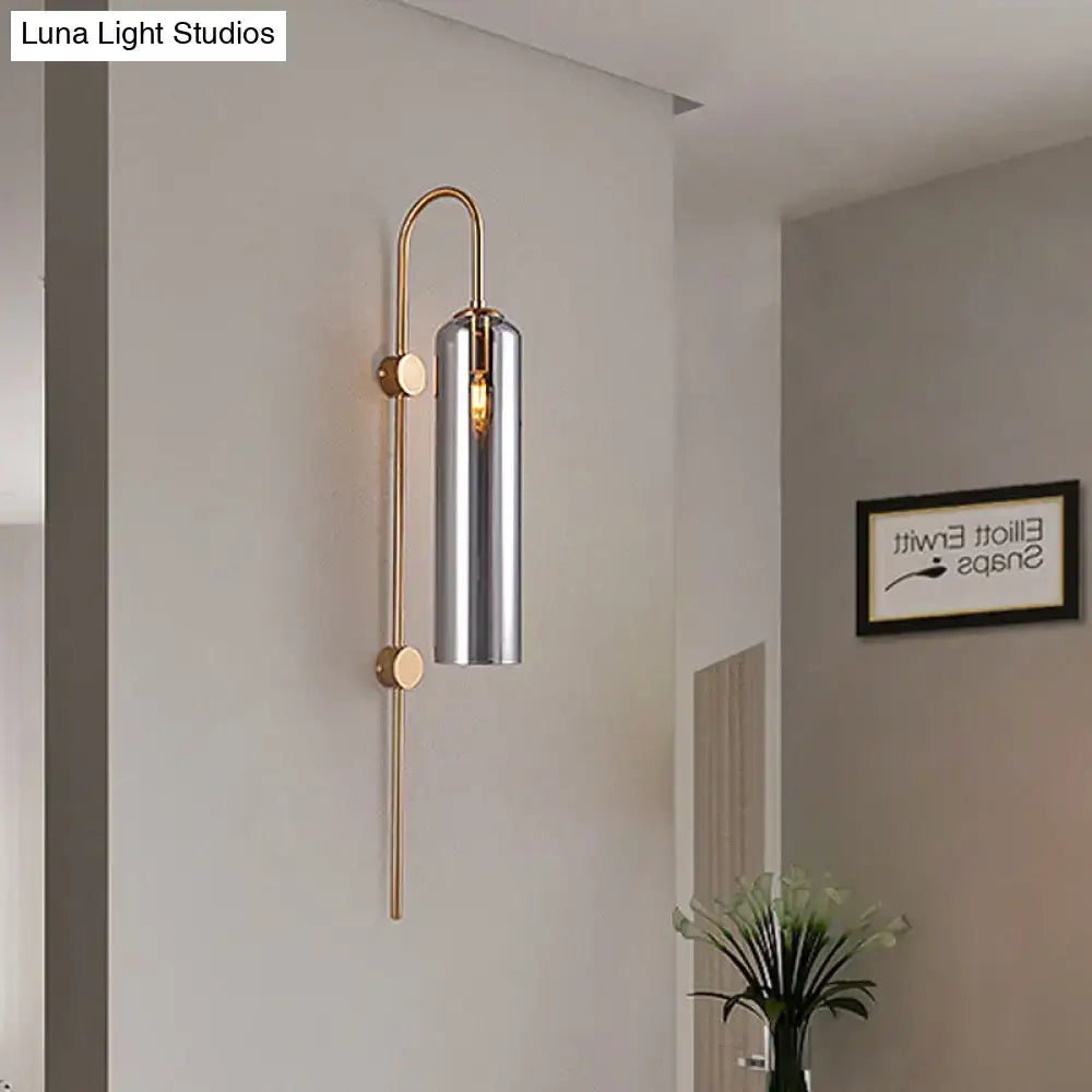 A modern smoke gray glass wall light with polished brass frame and cylindrical chrome shade for living room use