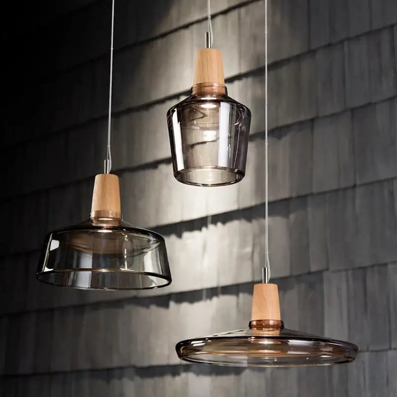 Three modern pendant lights with smoked glass shades and light wood accents hang against a dark shingled wall