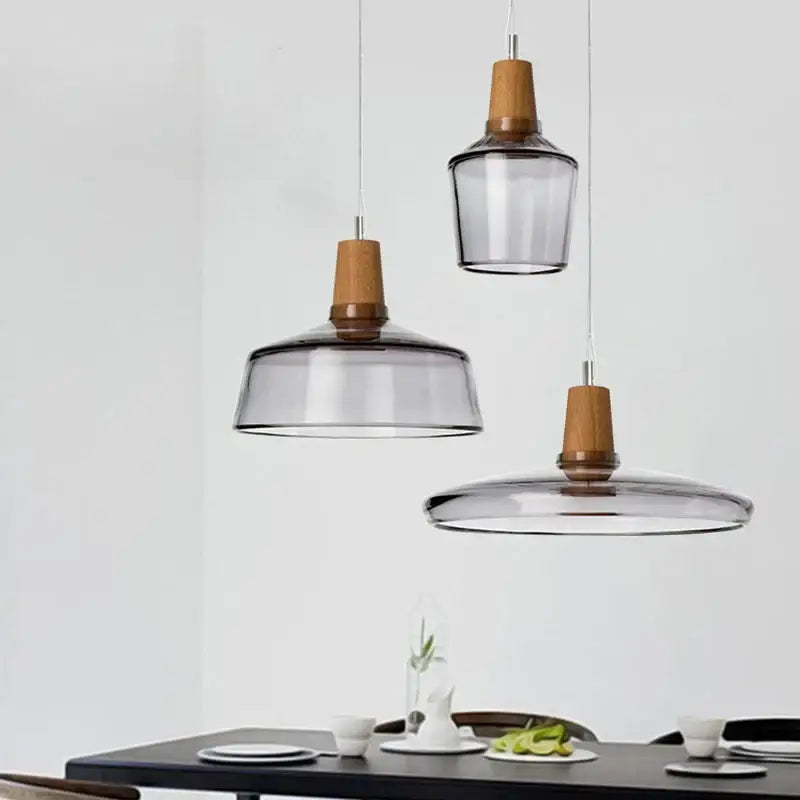 Three modern pendant lights with smoked glass shades and warm wood accents above a dining table