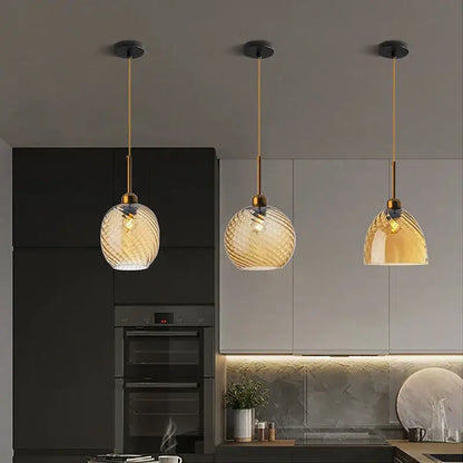 Three amber glass chandelier pendant lights with gold metal fixtures and swirling patterns for modern kitchen use