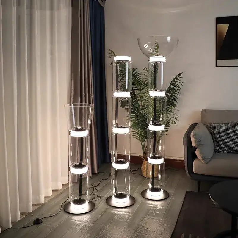 Three modern glass led floor lamps with stacked cylindrical transparent bodies and illuminated white led rings for living room lighting