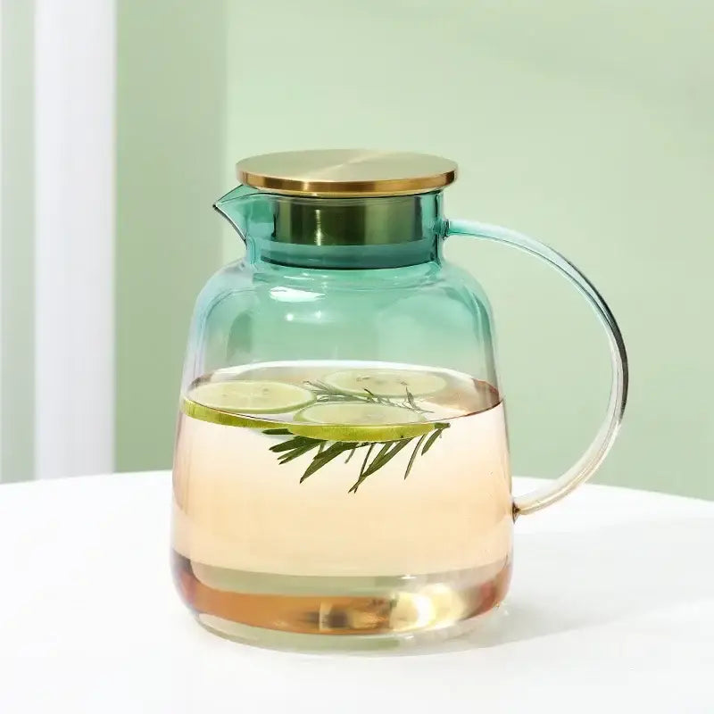 Modern teal and gold glass teapot set pitcher with a transparent glass body filled with infused water garnished with lime and rosemary