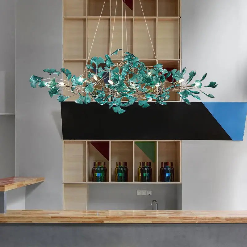 Modern teal glass gingko leaf chandelier with metallic branches suspended above wooden counter decorbites gingko leaf decor