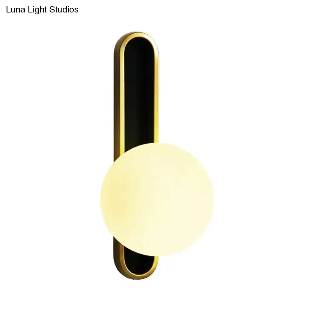 Modern teal and terracotta cylindrical side table next to a wall light orb wall with gold frame and off-white glass shade