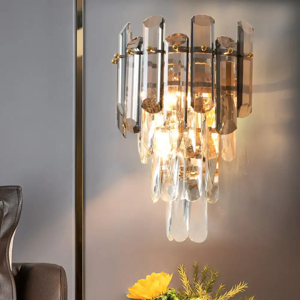 Modern tiered clear and smoke grey crystal wall sconce with vertical glass tubes and gold-toned hardware for bedroom lighting