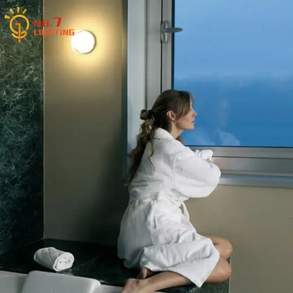 Woman in white plush robe sitting by bathtub next to modern translucent glass dimple potato chip wall lamp