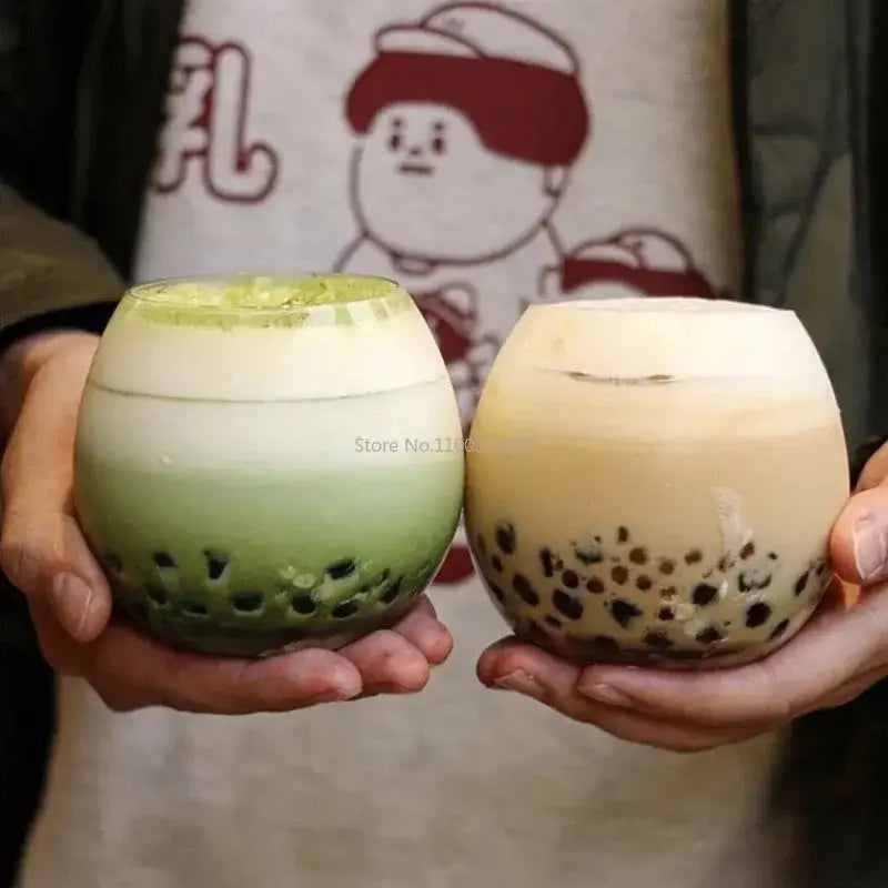 Two round clear plastic cups with layered bubble tea beside a modern transparent glass coffee mug for kitchen use