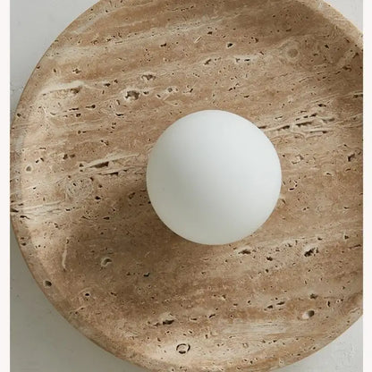 A smooth matte white travertine glass ball led ceiling light resting on a textured beige stone plate for bedroom decorbites decor