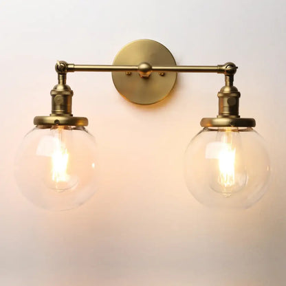 Brass-finished wall sconce with double ball heads glass globes and vintage edison bulbs for bedroom lighting