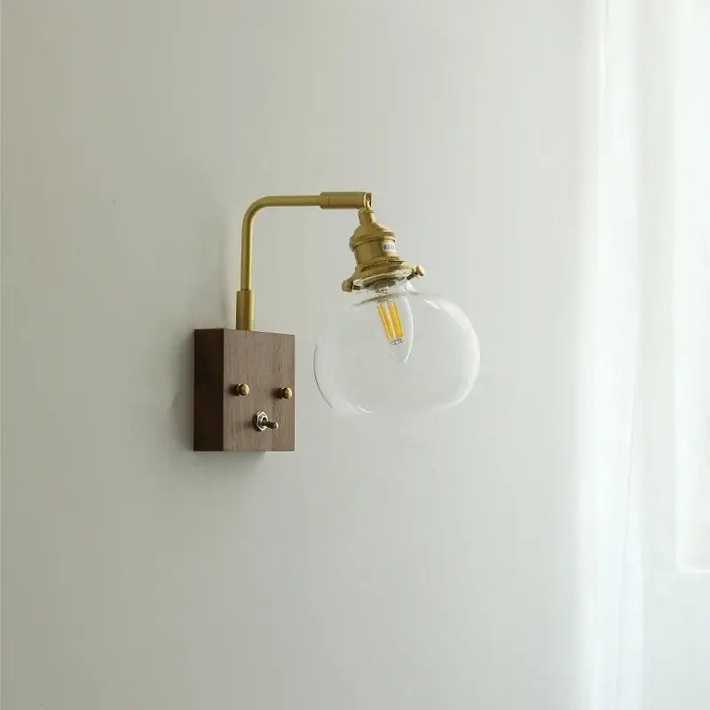 Modern walnut copper wall sconce with brass finish, wooden base, and clear glass globe housing led filament bulb