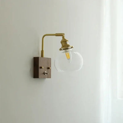 Modern walnut copper wall sconce with brass finish, wooden base, and clear glass globe housing led filament bulb