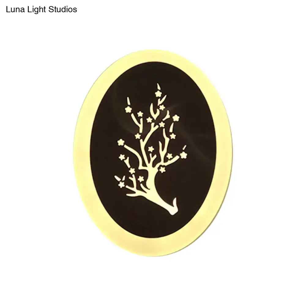An oval decorative plaque with a black center and white tree design framed by gold complementing a white acrylic wall lamp