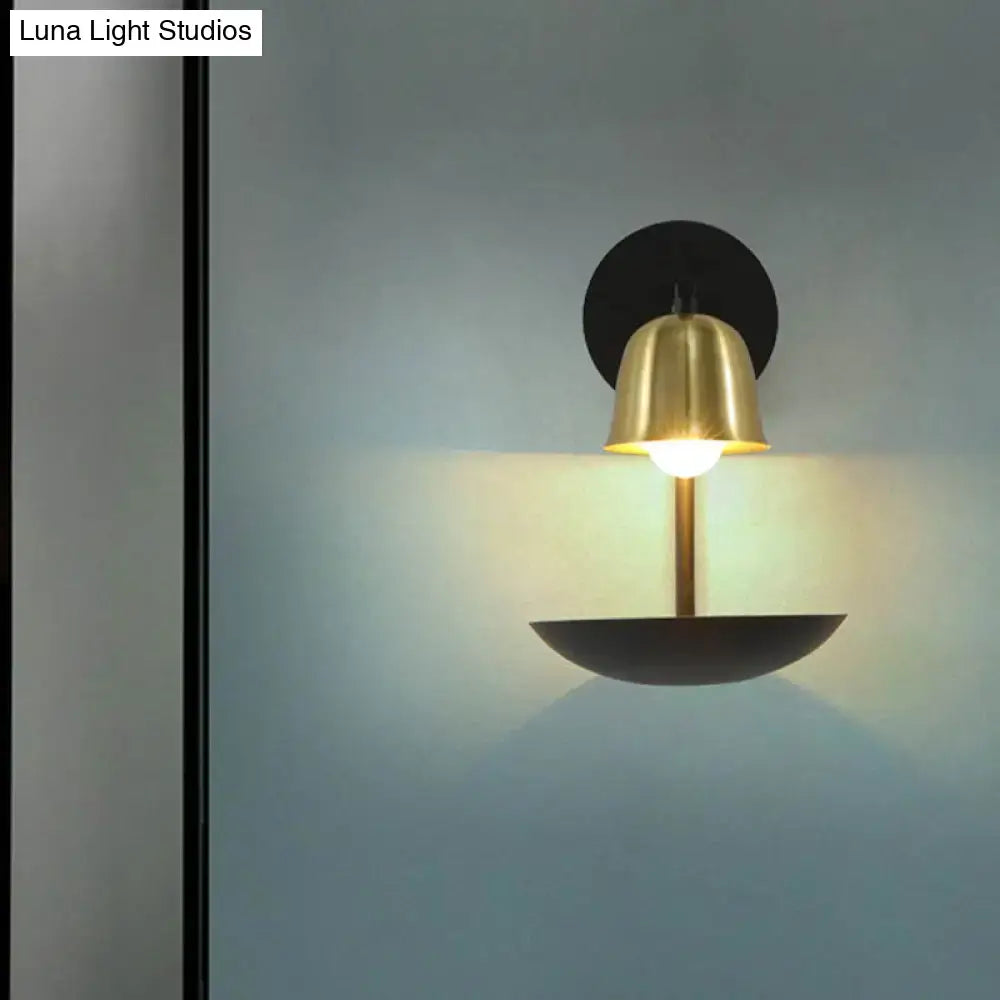 A modern white and brass bell metal sconce with polished brass shade and black base for elegant bedroom lighting