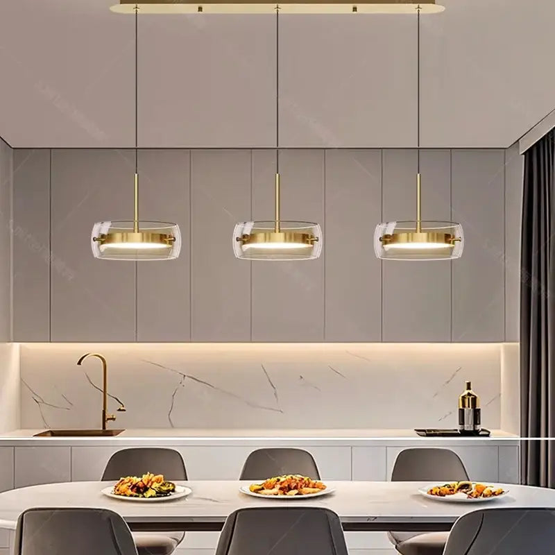 Three modern white pendant lights with clear glass shades and gold metal frames for remote dimming dining room use