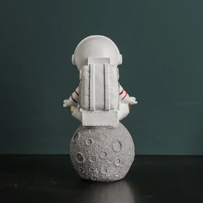 Modern white astronaut figurine with red stripes sitting meditative on textured gray moon electroplated golden decor