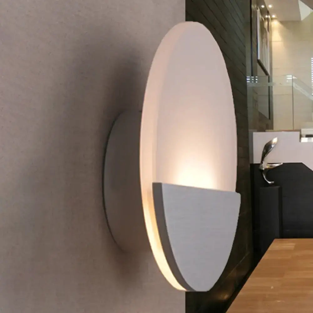Modern oval-shaped led sconce light in matte white with silver accents providing warm ambient glow for bedrooms