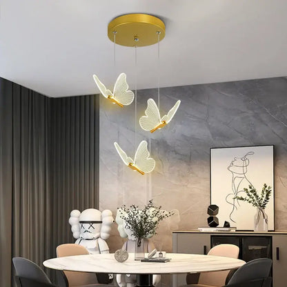 Three elegant white butterfly pendant lights with warm gold finish hang from a circular golden ceiling fixture