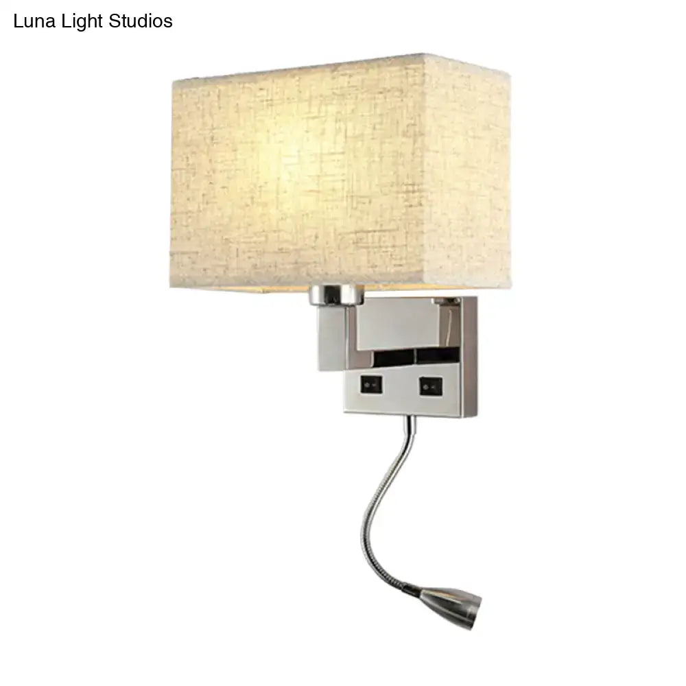 A modern wall-mounted lamp with a rectangular beige fabric shade and a sleek chrome-finished metal base, featuring an adjustable gooseneck reading light.