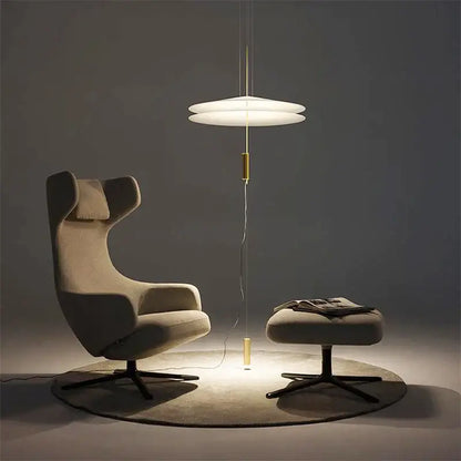 Modern beige upholstered armchair with wingback design and black metal base beside decorbites flying saucer pendant light
