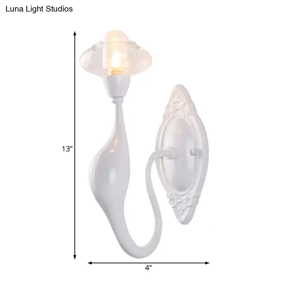 White ceramic sconce light with curved sculptural design and ornate backplate featuring clear glass oval for bedroom use