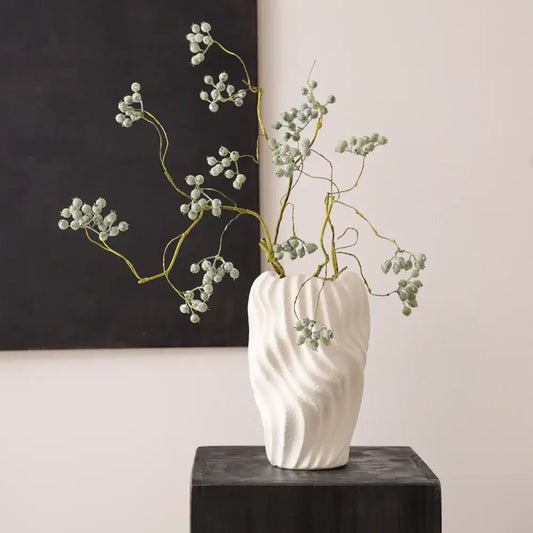 Modern white ceramic vase with irregular wavy patterns holding delicate green stems and light gray berries for decor