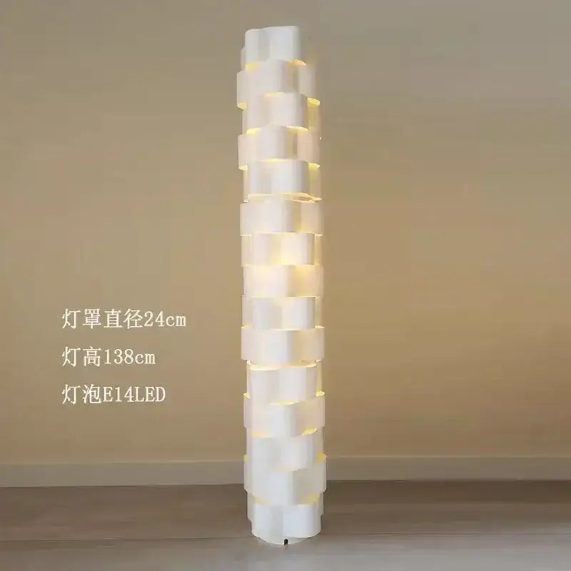 Modern white cylindrical vertical floor lamp with stacked geometric segments emitting warm light for living room use