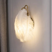 Modern white feather metal wall sconce with a luminous white feather and gold-toned metal frame for bedroom lighting