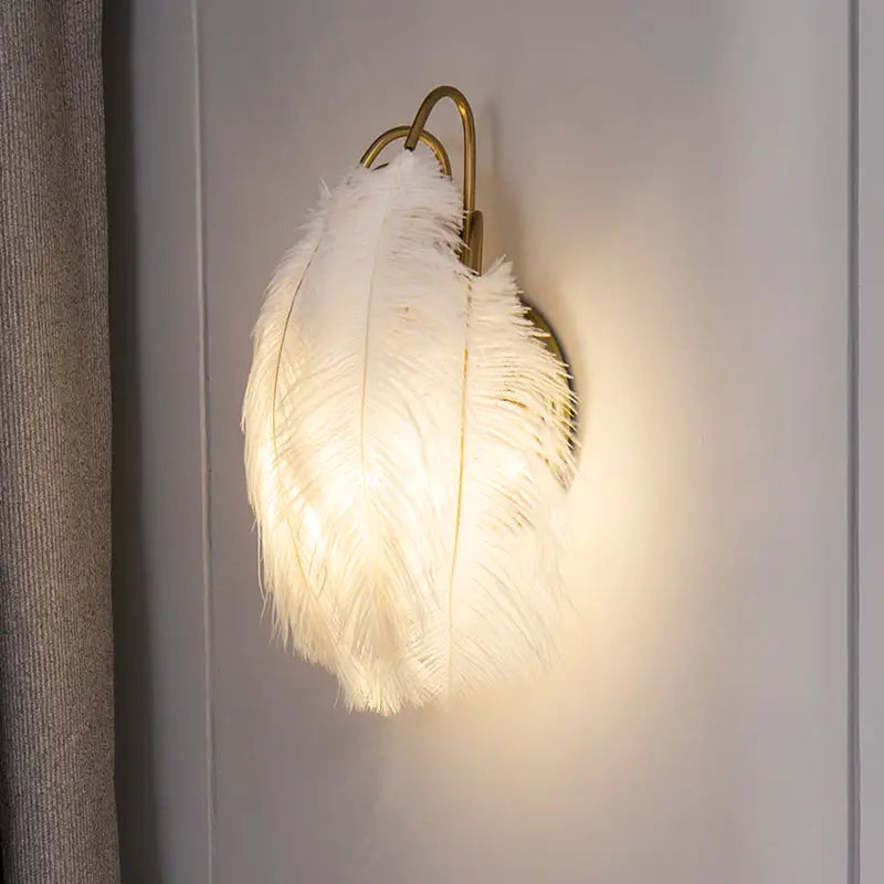 Modern white feather metal wall sconce with a luminous white feather and gold-toned metal frame for bedroom lighting