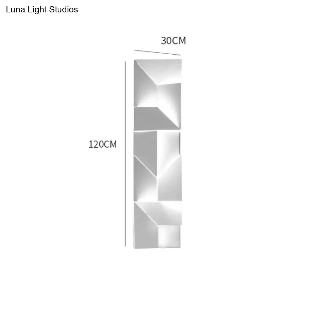 A sleek modern white geometric wall lamp in polished metal illuminating a living room with art design
