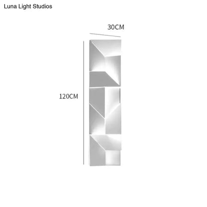 A sleek modern white geometric wall lamp in polished metal illuminating a living room with art design