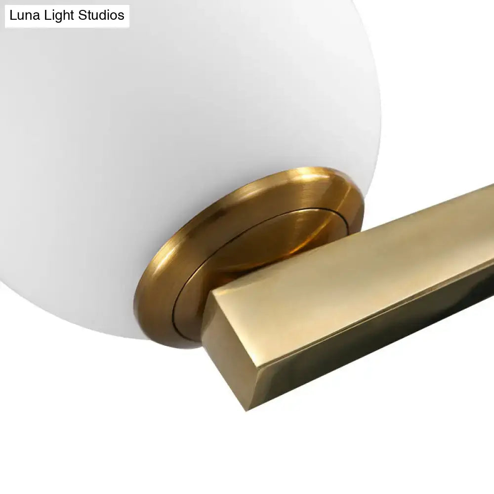 A modern single light wall light with a frosted white glass globe and polished brass arm for bedroom use