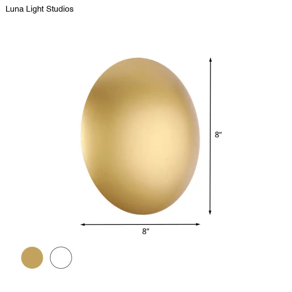 Gold-colored oval wall light with smooth metallic finish in white gold providing warm white illumination for bedrooms