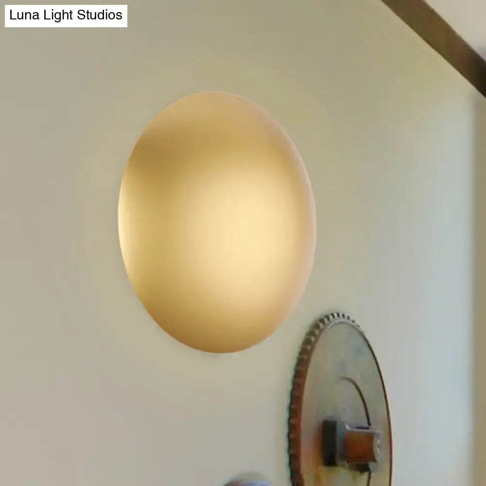 A sleek gold-toned circular wall light with matte finish providing warm white illumination for bedrooms