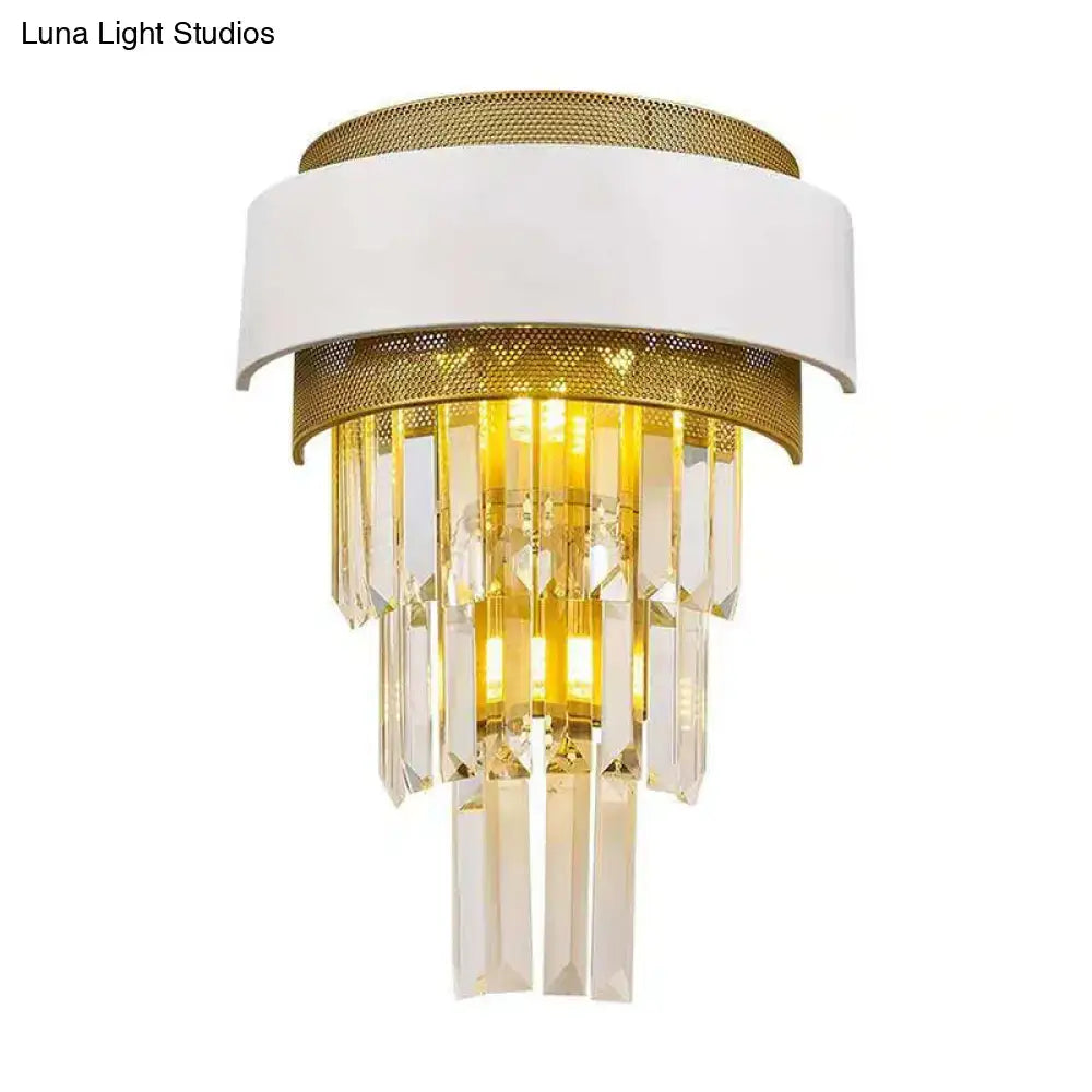 Modern wall sconce with white and gold metallic frame and cascading clear crystal prisms emitting warm light