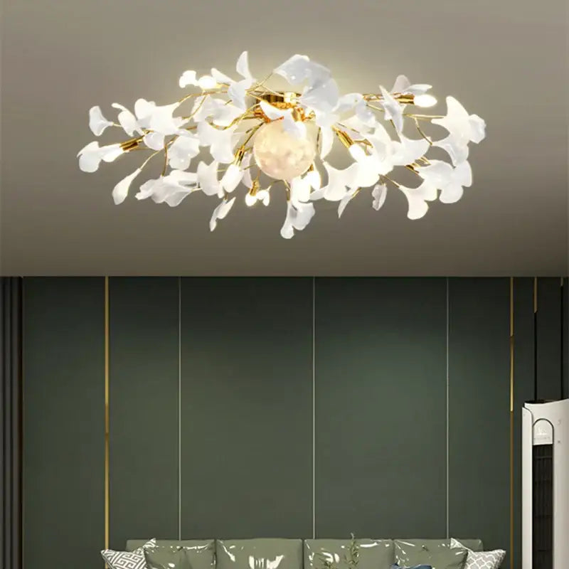 A modern white and gold ginkgo leaf led ceiling chandelier with delicate glass petals and a warm glowing bulb