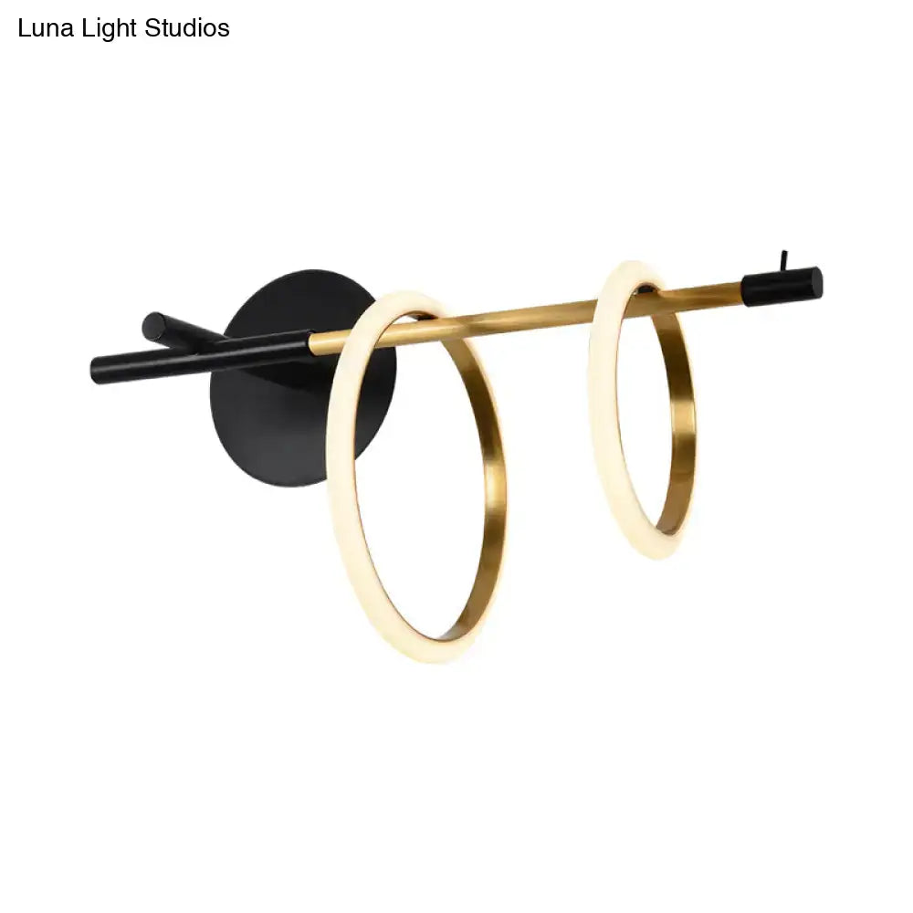 Modernist wall light featuring two glowing gold rings on a black and brass bar in a living room light fixture