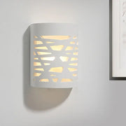 Modern white cylindrical wall sconce with geometric cutout pattern casting warm light from led light bulb