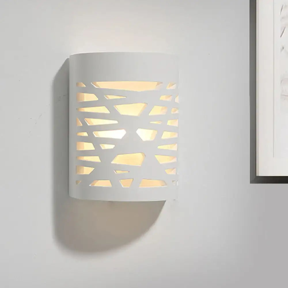 Modern white cylindrical wall sconce with geometric cutout pattern casting warm light from led light bulb
