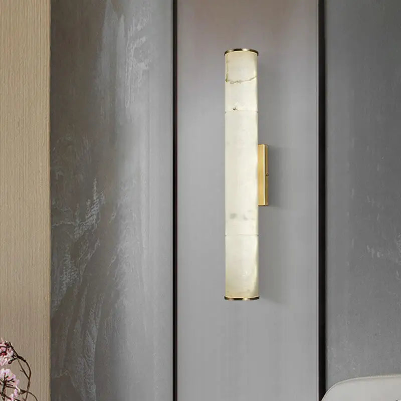A modern white marble and brass wall lamp with a cylindrical fixture height for living room lighting