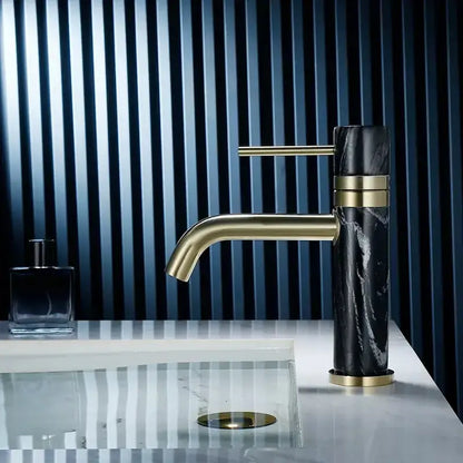 A modern white marble and black marble bathroom faucet with brushed gold swivel spout and decorbites brushed gold trim