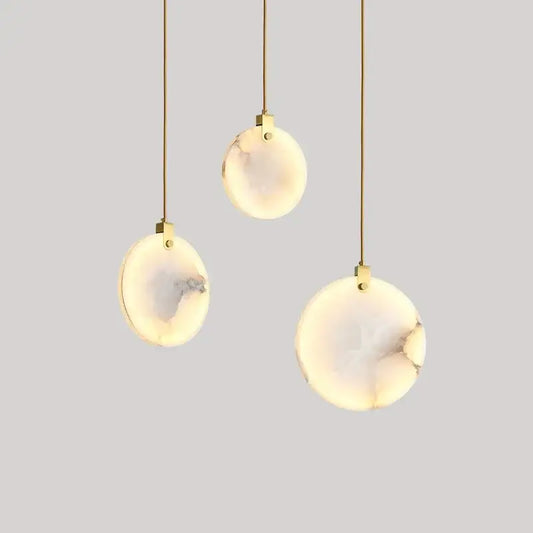 Three elegant marble pendant lights with warm opal stone shades and gold-toned cords for dining room use