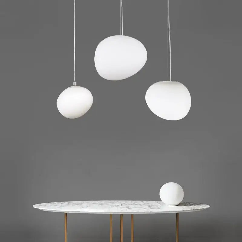 Modern white matte glass pendant lights with egg-shaped design hanging above a marble table for living room use