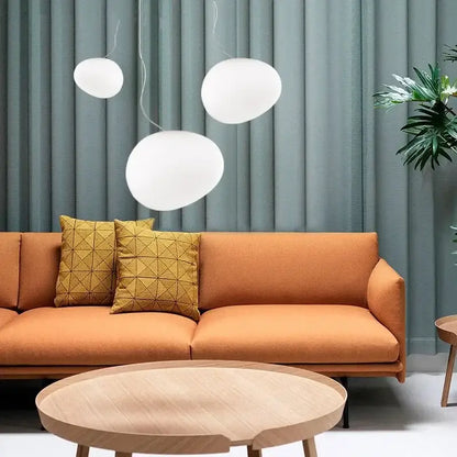 Three white matte glass pendant lights hanging above a modern orange sofa in a living room setting
